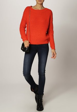 Red knitted sweater with a textured pattern, round neckline, and relaxed fit, paired with dark skinny jeans and black ankle boots.