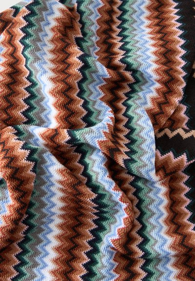 Tissu tricoté doux avec motif en zigzag dans les couleurs marron, bleu, vert, blanc et noir, présenté avec des plis et des détails de texture.