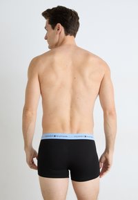 Fekete boxer alsónadrág világoskék derékszíjjal, amelyen a "TOMMY HILFIGER" logó látható. A modell hátulról látható, semleges háttérrel.