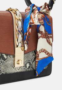 Sac à main texturé marron et noir avec une chaîne dorée, un fermoir doré et un foulard à motifs bleu, blanc et marron attaché à la poignée.