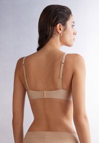 Beige bra with adjustable straps and a hook-and-eye closure. Smooth fabric with a seamless design, shown from the back.