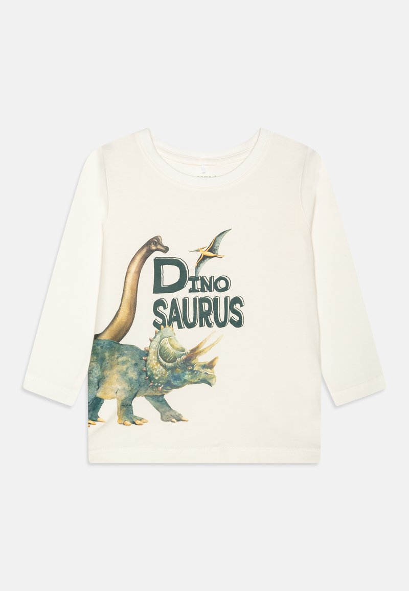 Maglietta a maniche lunghe color crema realizzata in tessuto morbido, con illustrazioni di dinosauri colorati e la scritta "DINO SAURUS" in lettere grasse di colore verde scuro.