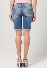 Bermudas de mezclilla en azul claro con puños enrollados, que cuentan con dos bolsillos traseros con detalles de costura clara. Se llevan con sandalias de tacón alto con estampado.