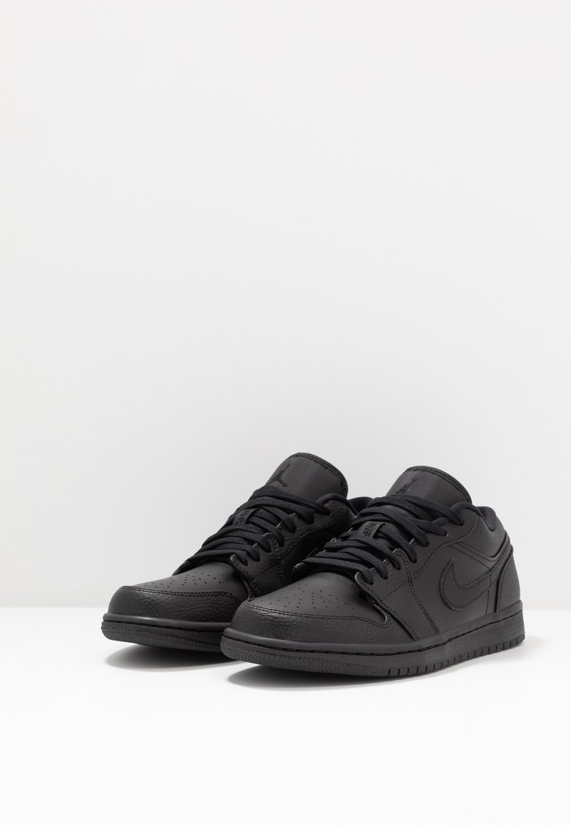 Schwarze Ledersneaker mit niedrigem Profil, perforiertem Zehenbereich, strukturierten Überzügen und tonal gestaltetem Branding auf der Zunge und der Seite.
