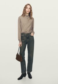 Jasnobrązowa koszula z długim rękawem z detalem z guzików, noszona z ciemnymi dżinsami i czarnymi botkami, trzymająca małą brązową torebkę.