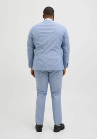 Helle blaue Sakkos und passende Hosen aus strukturiertem Stoff. Das Sakko hat einen einzelnen Schlitz und schwarze Knöpfe, kombiniert mit dunklen Schuhen.