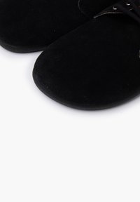 Czarne zamszowe buty z okrągłymi noskami i płaską podeszwą. Posiadają sznurówki i gładką fakturę. Zbliżenie podkreśla materiał i design.