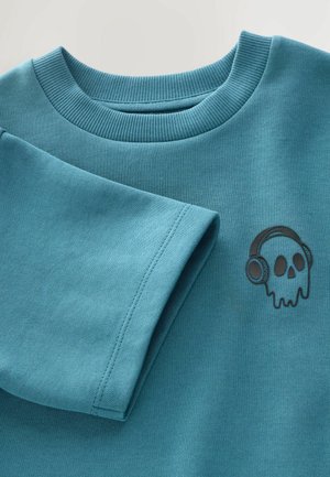 Sweatshirt teal avec un col ribbed et un graphique d'un crâne avec des écouteurs sur la poitrine. Le tissu a une finition lisse et texturée.