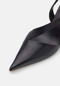 Chaussure noire en cuir à bout pointu avec un design croisé sur le dessus. Texture élégante et finition lisse. Style minimaliste avec un aspect slingback.