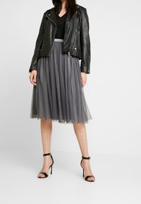 Zwarte leren motorjack gecombineerd met een grijze tule midi-jurk en zwarte gespsandalen. De jurk heeft een geplooide textuur.