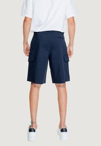 Pantaloni cargo navy con due tasche laterali, fronte piatto e tasca sul retro, realizzati in tessuto leggero, abbinati a sneakers bianche.