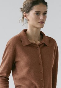 Bruine cardigan gemaakt van zacht materiaal, met een kraag, knoopsluiting aan de voorkant en lange mouwen. Soepele textuur en een getailleerde pasvorm.