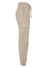 Pantalon cargo beige avec taille élastique et poignets aux chevilles, poches latérales et une poche à rabat sur la cuisse.