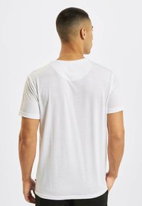 Valge puuvillane T-särk lühikeste varrukatega, ümmargune kaelus ja sile tekstuur. Tagantvaates on lihtne disain ilma graafikateta.