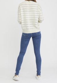 Jersey a rayas de colores claros con acentos metálicos, combinado con jeans oscuros de corte ajustado y zapatillas blancas con detalles en dorado.