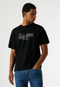 Černé bavlněné tričko s kulatým výstřihem a krátkými rukávy, s výrazným bílým potiskem loga "PEPE JEANS LONDON" a opotřebovanými detaily.