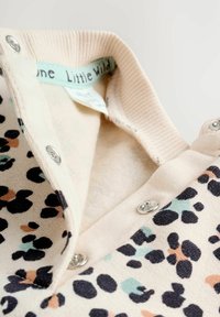Sweatshirt imprimé léopard avec une base crème, boutons-pression et une doublure intérieure douce et texturée. Col côtelé et étiquette menthe légère visible.