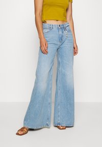 Lichtblauwe jeans met wijde pijpen en een verweerde look, voorzien van twee steekzakken aan de voorkant, metalen details en subtiele stiknaden.