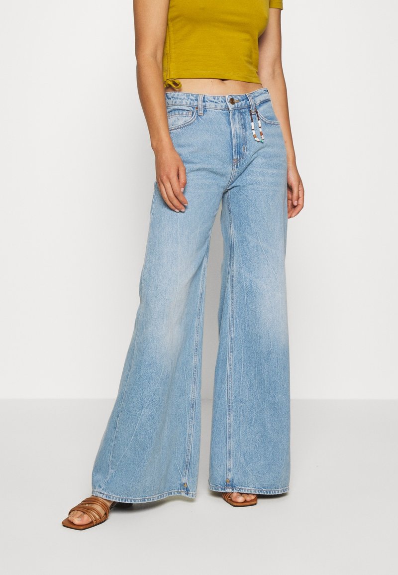 Lichtblauwe jeans met wijde pijpen en een verweerde look, voorzien van twee steekzakken aan de voorkant, metalen details en subtiele stiknaden.