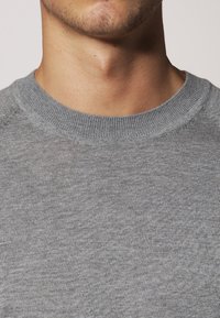 Grauer gestrickter Pullover mit einem gerippten Rundhalsausschnitt und subtiler Textur. Der Stoff wirkt weich und körpernah, ohne sichtbare Logos oder Muster.