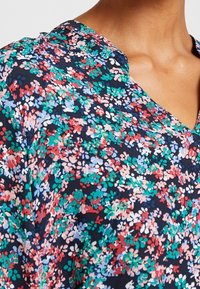 Blusa floreale in tessuto blu navy, con piccoli fiori multicolori in rosa, verde e blu. Design a V con texture morbida.