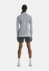 Helles graues Langarmoberteil mit flachen Nähten, kombiniert mit dunklen Shorts. Das Outfit besteht aus feuchtigkeitsableitendem Material und verfügt über ein körperbetontes Design.