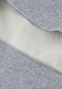Tejido de sudadera gris superpuesto sobre un suave forro polar blanco. Punto gris texturizado con costuras visibles en el borde, creando un acabado limpio.