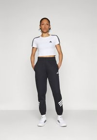 Λευκό cropped t-shirt με μαύρες ρίγες στους ώμους, συνδυασμένο με σκούρο γκρι παντελόνι φόρμας με λευκές τρεις ρίγες και ελαστικές μανσέτες.