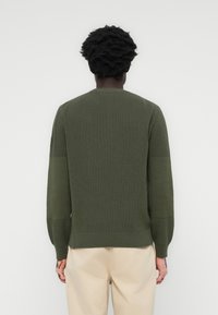 Green knitted sweater with a crew neck, ribbed texture, long sleeves, and a fitted hem. The design features contrasting fabric on the sleeves.