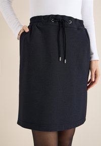 Marineblauer Rock mit elastischem Bund, Kordelzugdetail und Seitentaschen; strukturierter Stoff mit dezentem Muster; knielanger Schnitt.