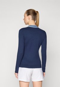 Marineblauwe geribbelde gebreide trui met een aansluitend ontwerp, voorzien van een contrasterende blauw-witte gestreepte kraag. Glad textuur, lange mouwen.