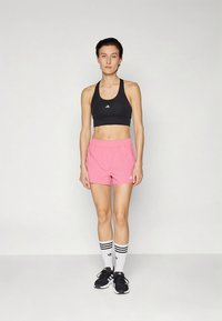 Black sports bra with white logo, pink shorts with elastic waist, black sneakers, and white socks with black stripes. Simple athletic attire.