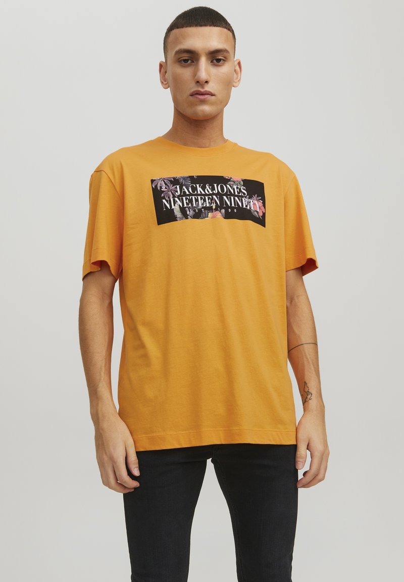 T-shirt di cotone arancione con grafica nera e dettagli floreali e testo "JACK & JONES NINETEEN NINETY." Vestibilità rilassata, maniche corte.