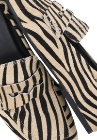 Mocassini con stampa zebra caratterizzati da una tomaia in pelliccia testurizzata beige e nera, con suola piatta in gomma a contrasto e dettagli decorativi con fibbie.