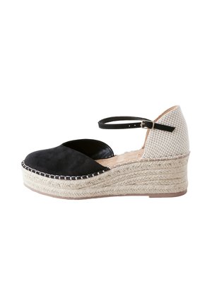 Sandale espadrille compensée avec bout fermé noir, talon beige tissé, semelle en jute et fine bride noire à la cheville avec boucle dorée.