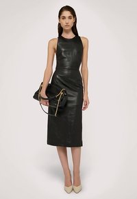 Svart läderklänning med figursydd överdel och midi-längd. Har en hög halsringning och slät textur, kompletterad med en svart handväska med gulddetaljer.