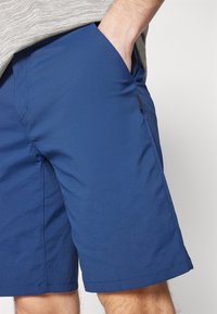 Blue shorts with a smooth, lightweight fabric. Features side pockets, a straight cut, and a short hem. Black tag visible on the side.