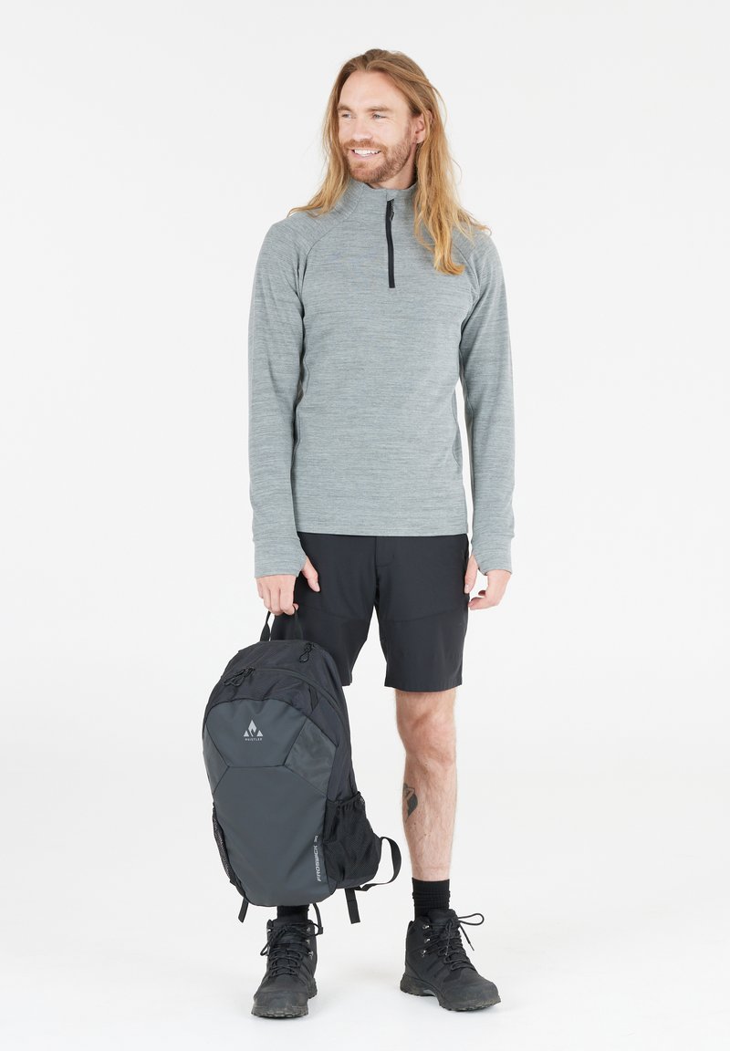 Szary długi rękaw pulower z ćwierć zamkiem, czarne szorty i czarny plecak z siateczkową kieszenią boczną. Czarne buty trekkingowe dopełniają strój.