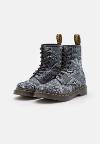 Botas de cordones con estampado de serpiente en blanco y negro, suela gruesa, costuras amarillas y tiradores, fabricadas con un material sintético texturizado.