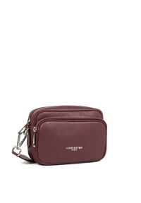 Borsa a tracolla in pelle bordeaux con due scomparti con zip, hardware argentato e logo "Lancaster Paris" in rilievo sulla parte anteriore.