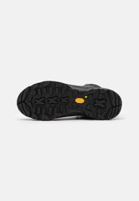 Suela de goma negra con patrones de relieve profundos y agresivos, que presenta un logo de Vibram y un talón elevado para mejorar el agarre y la tracción.