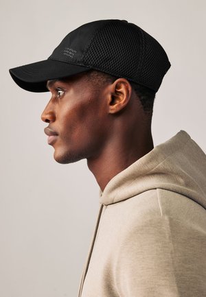 Must mustvalge pesapalli nokamüts võrguga külgedel ja kõverdatud nokaga, väikese logoga ees. Kantakse beeži kapuutsiga.