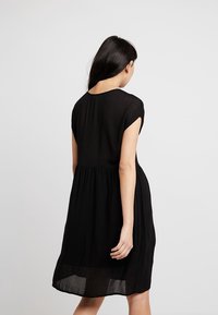 Schwarzes Kleid aus leichtem Stoff, mit kurzen Ärmeln, einem runden Ausschnitt und einer gerafften Taille, die bis zum knie-langen Saum fließt.