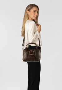 Borsa a mano in pelle marrone con un accento circolare dorato sul fronte, doppi manici e una tracolla staccabile, mostrata su uno sfondo neutro.