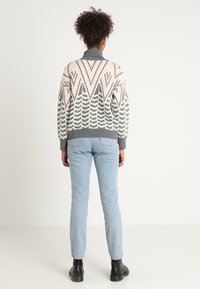 Flerfärgad stickad tröja med geometriskt mönster i rosa, grått och krämfärgat, tillsammans med ljusblå jeans och svarta ankelstövlar.