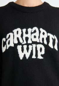 Czarny sweter z dzianiny z białym, puszystym wzorem graficznym z napisem "carhartt WIP" w pogrubionych, zaokrąglonych literach na piersi.