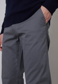Gray cotton trousers with a straight fit, featuring side pockets and minimal seam detailing. Worn with a dark navy sweater.