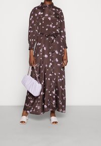 Braun bedrucktes Kleid mit langen Ärmeln und Kragen, in der Taille gebunden. Kombiniert mit einer hell-lavendel Farbe Tasche und hellen offenen Schuhen.