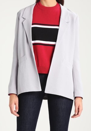 Hellgrauer Blazer mit lockerer Passform, mit Revers und zwei vorderen Taschen, getragen über einem rot-schwarz-weißen gestreiften Pullover.