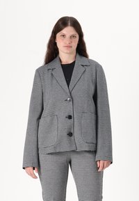 Svart-hvitt rutet blazer med ensidig design, kile-lapper, tre knapper og to frontlommer, kombinert med matchende bukser.